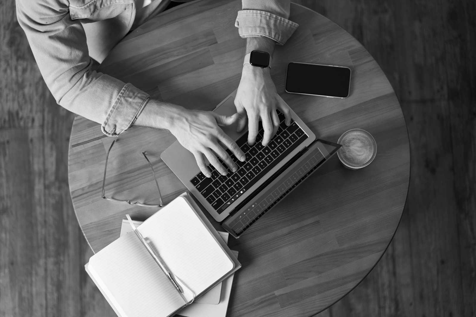 Person tippt am Laptop auf runden Tisch; Notizbuch, Smartphone, Kaffee - Fokus auf elektronik und embedded software